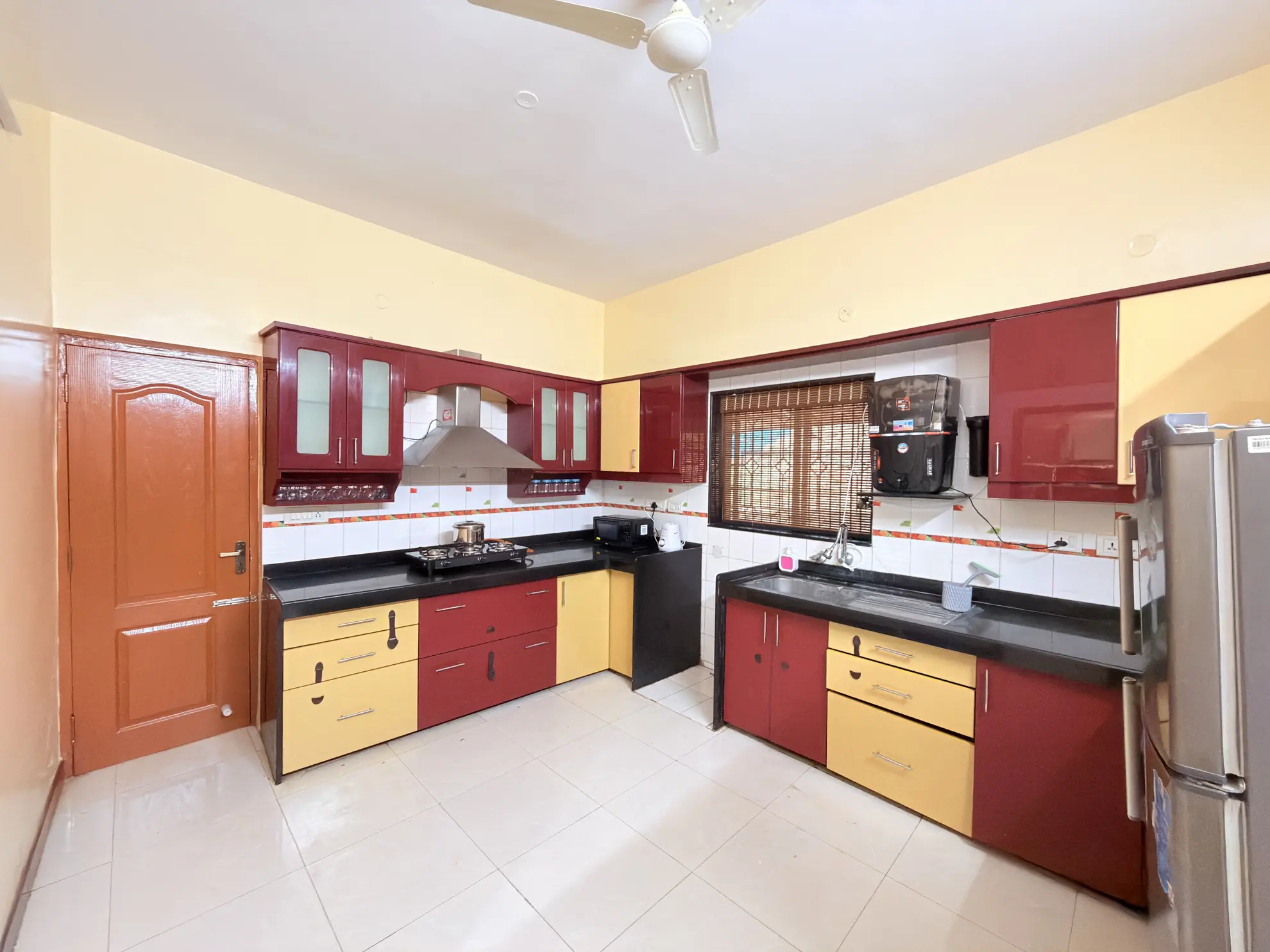 Bright L-shaped kitchen with red and yellow cabinets, black countertops, gas hob, and stainless fridge.