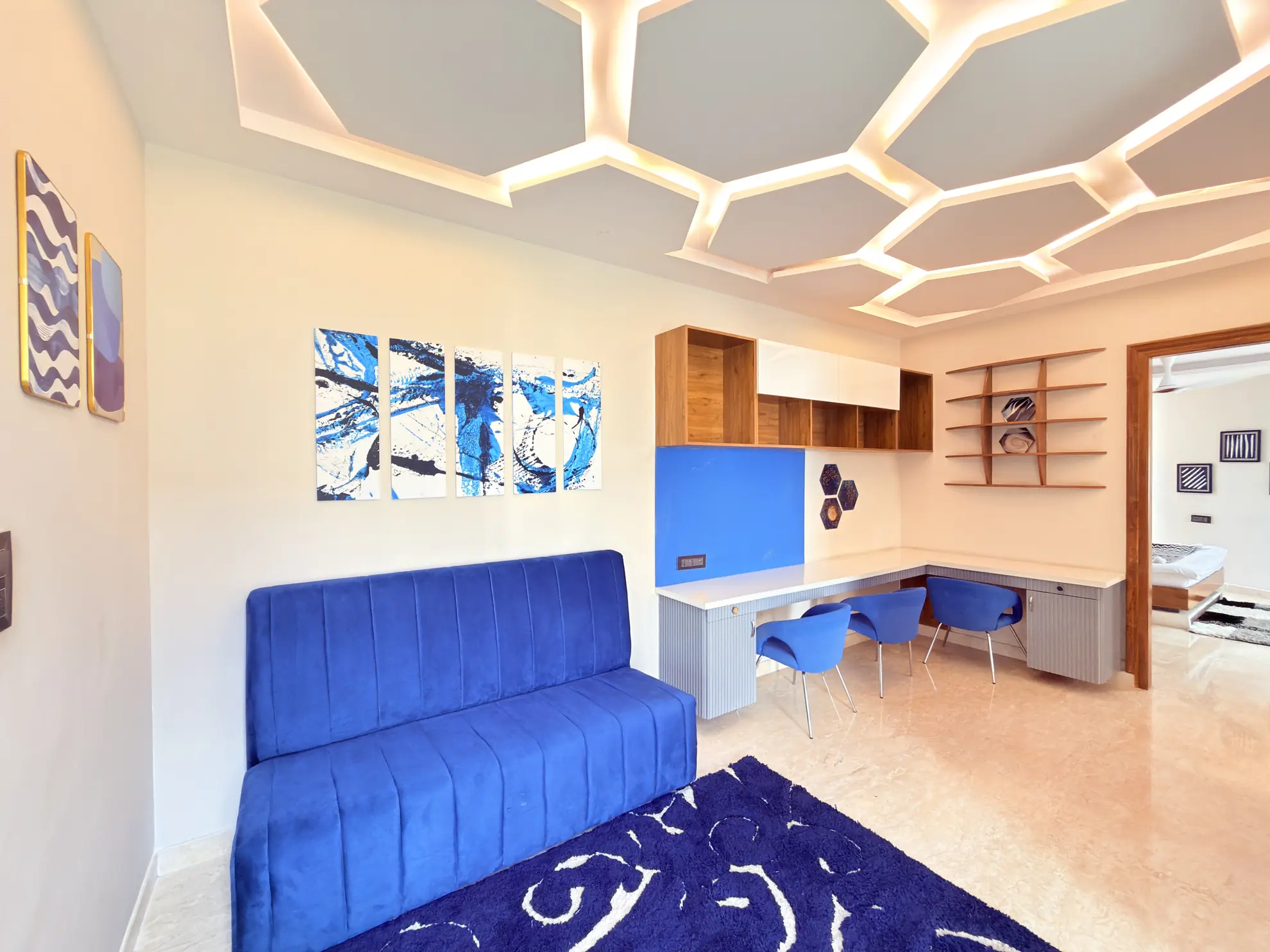 Blue velvet bench seat beside a built-in desk with six chairs, under a backlit honeycomb ceiling.
