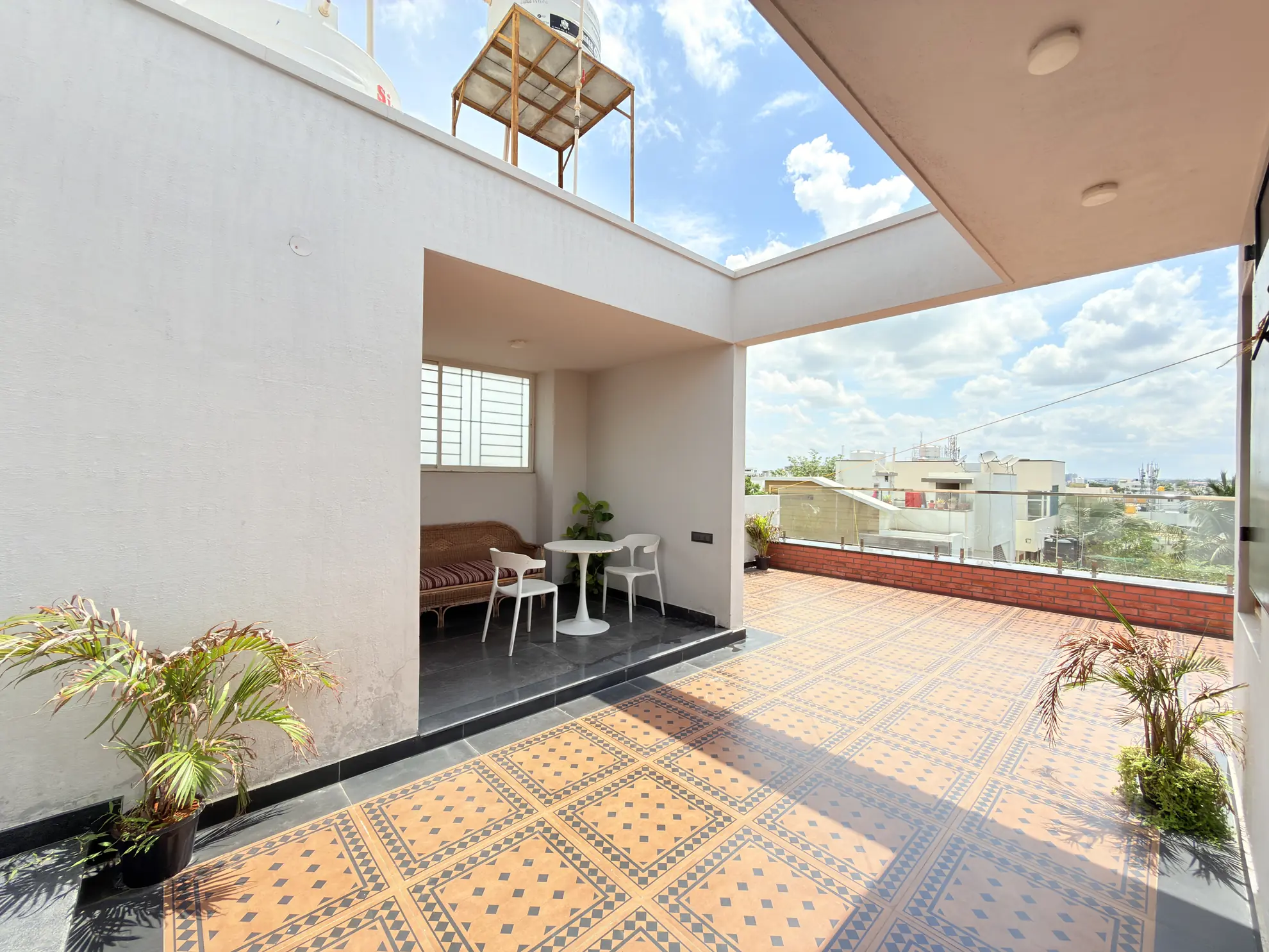 Open rooftop terrace with patterned tiles, a small white bistro table with two chairs, and a wicker bench under an overhang.