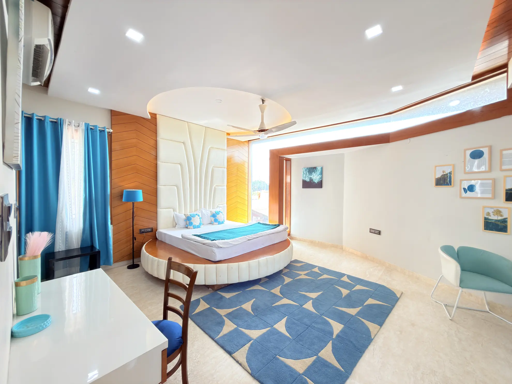 Bedroom with a round platform bed, blue geometric rug, and teal armchair beside wall art.