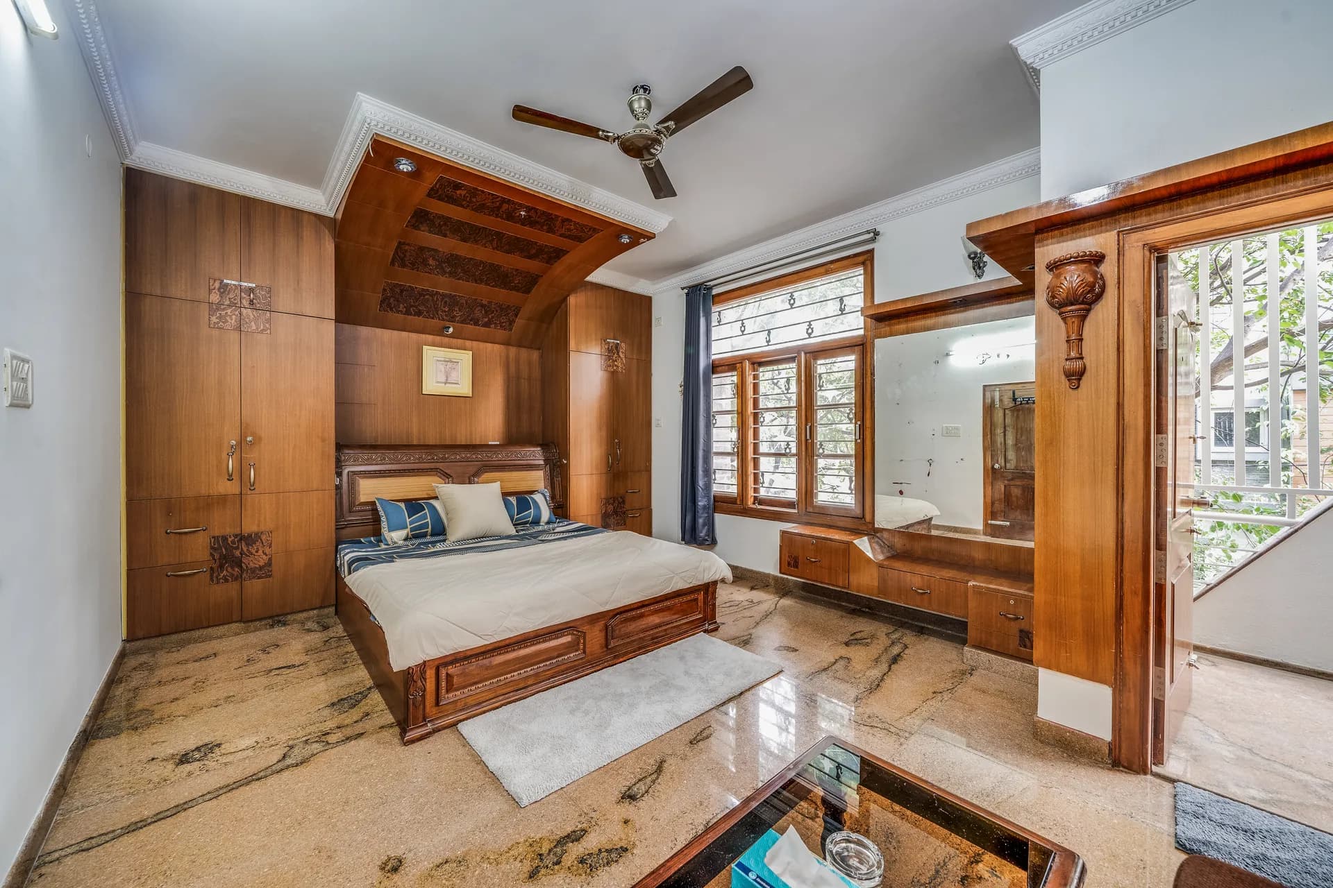 Bedroom with a wood-panelled bed alcove, built-in wardrobes, a ceiling fan and marble floor.